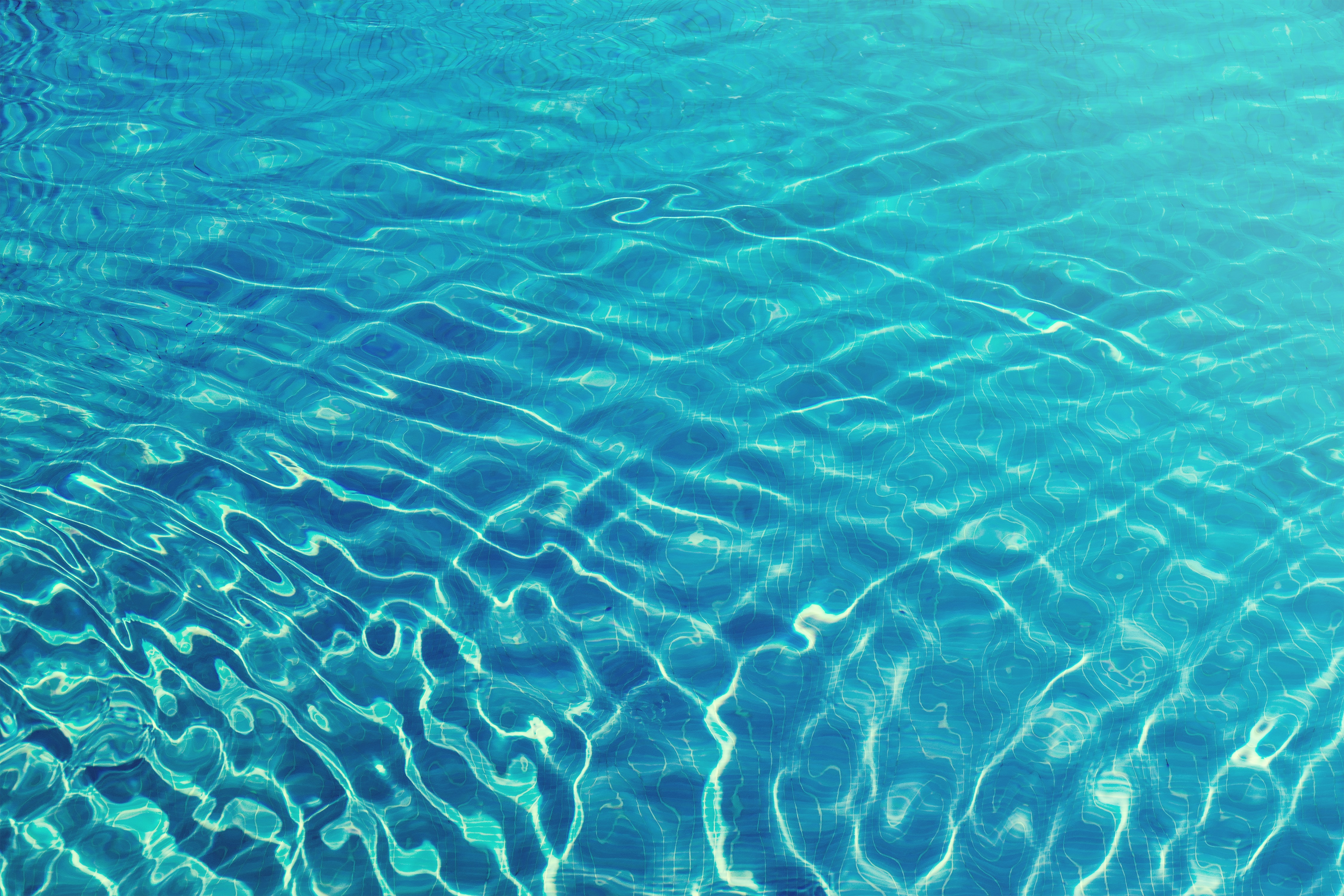 A foto mostra uma piscina, mas o foco está somente na água, com uma luz do sol refletindo.