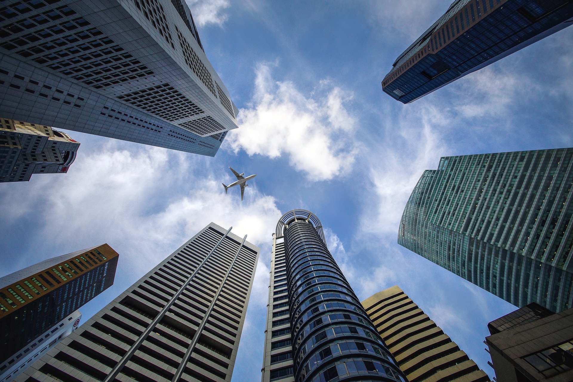 Imagem feita de baixo para cima mostrando vários prédios e um avião passando no céu