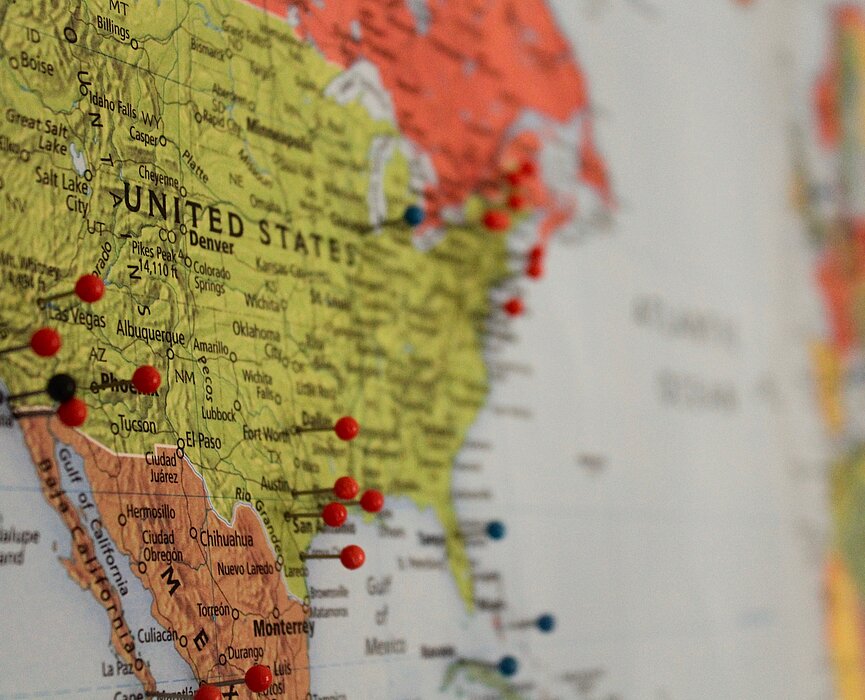 A imagem mostra um mapa, com os Estados Unidos em evidência e alguns alfinetes grudados em determinados locais. 