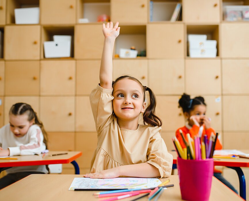Garota em sala de aula com a mão levantada sentada na sua carteira