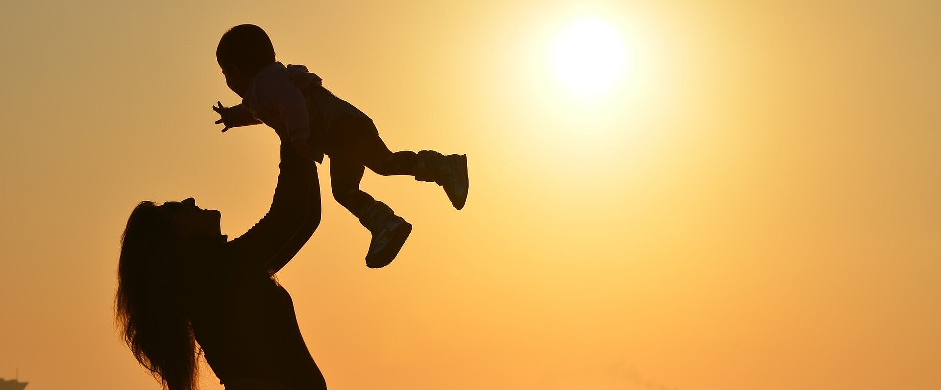 mulher segura seu filho no alto na praia com por do sol ao fundo