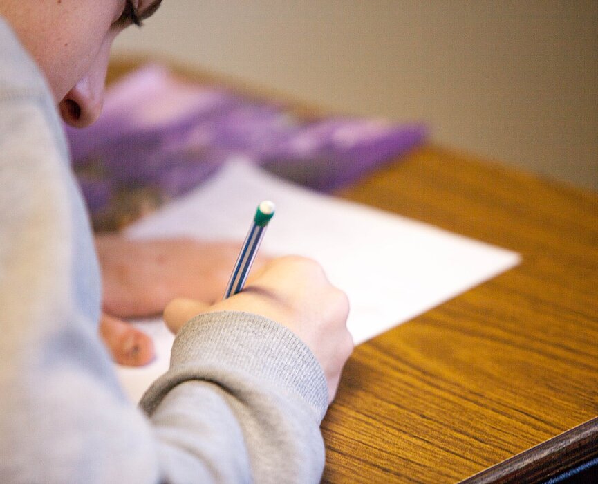 menina debruçada sobre uma folha de prova com o lápis na mão e concentrada no teste