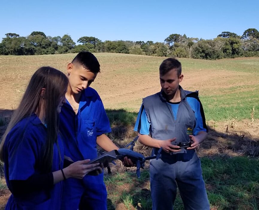 Três pessoas em uma fazenda com um drone na mão 