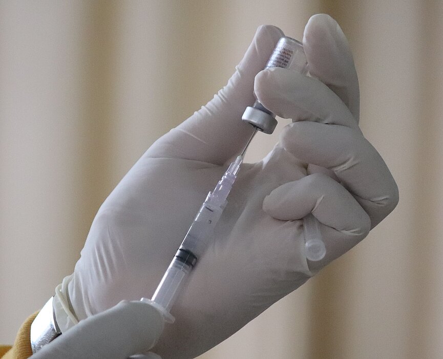 Mão de profissional da saúde segurando uma dose da vacina 