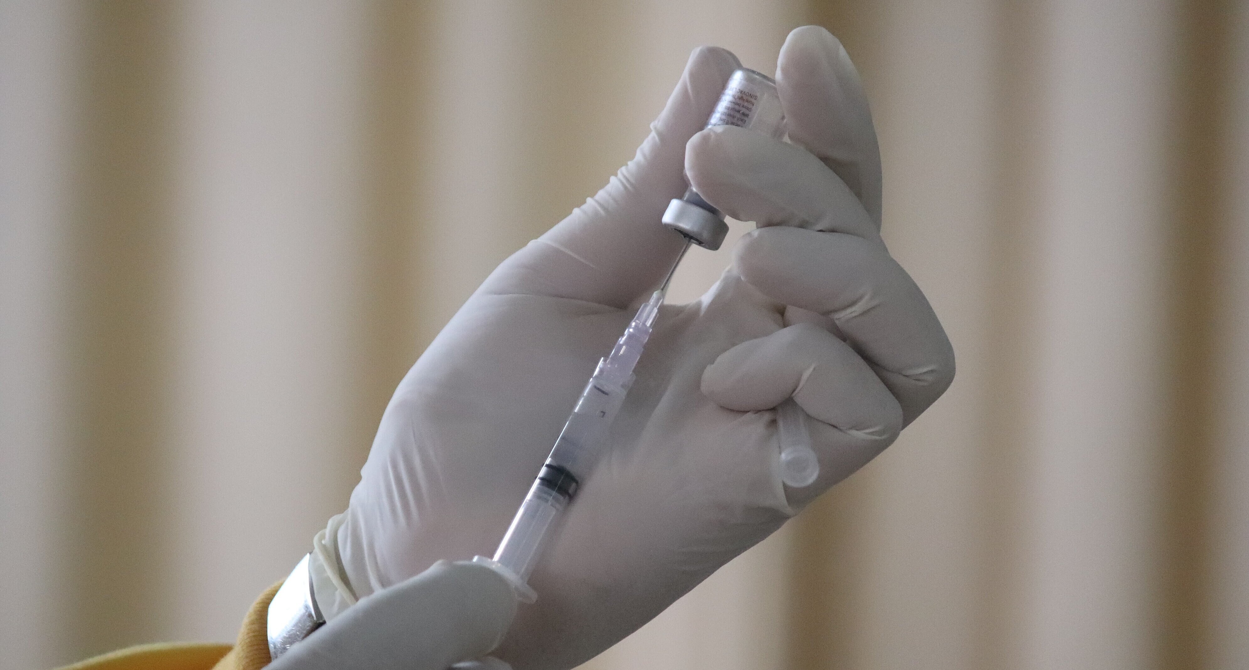 Mão de profissional da saúde segurando uma dose da vacina 