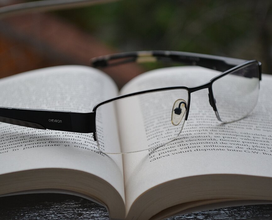 Imagem com um livro aberto e um óculos de grau em cima