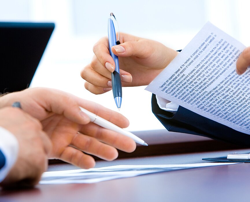 Mãos segurando canetas com documentos sobre a mesa