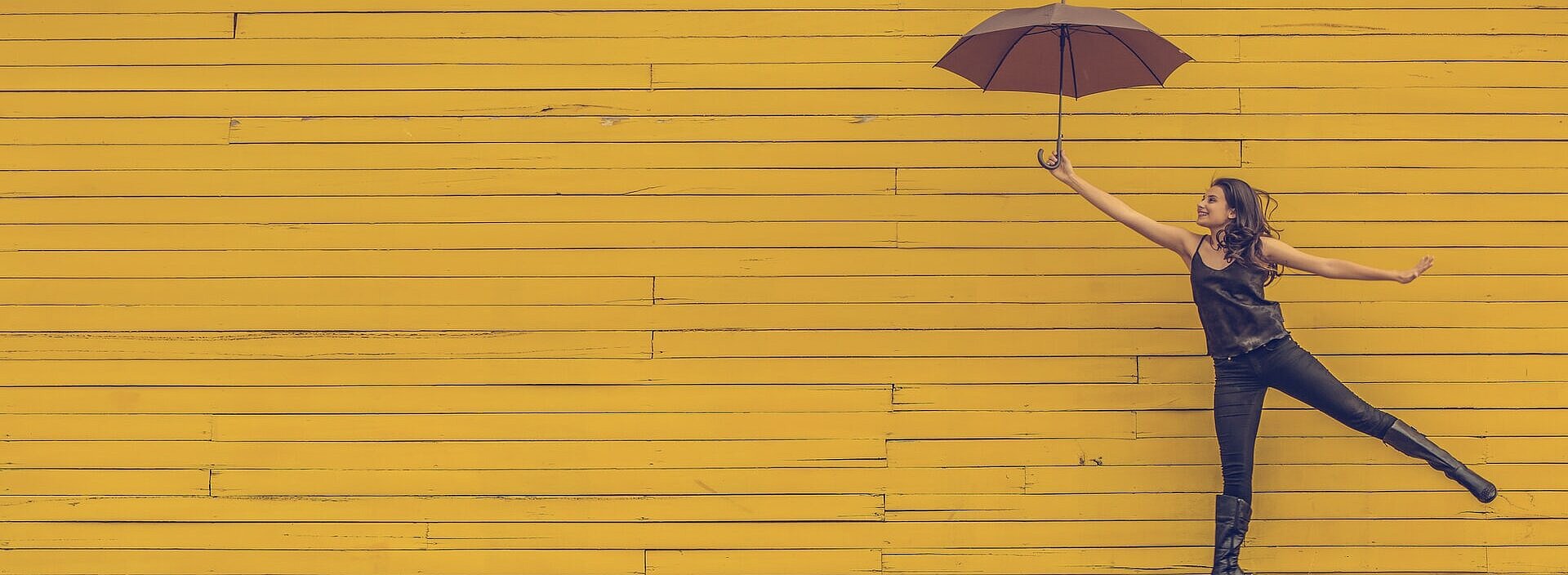 mulher segurando um guarda-chuva e pulando em um fundo de parede amarela
